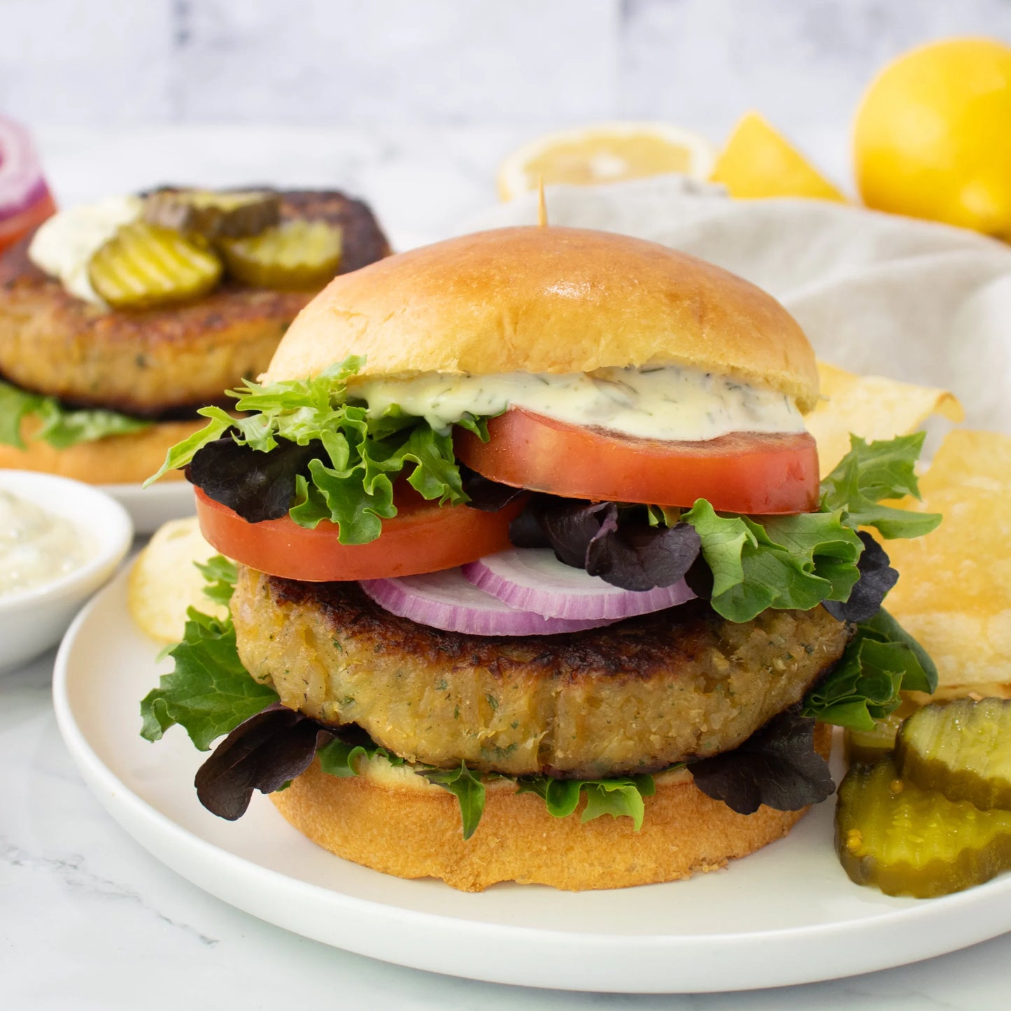 Deliciously prepared crab cake burger with various toppings on a white plate, set against a neutral background.